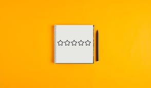 A notebook with 5 stars on it is shown next to a pen against a tangerine orange background