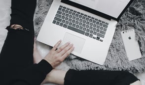Lady dressed in black jeans working on her laptop while sitting on her grey rug