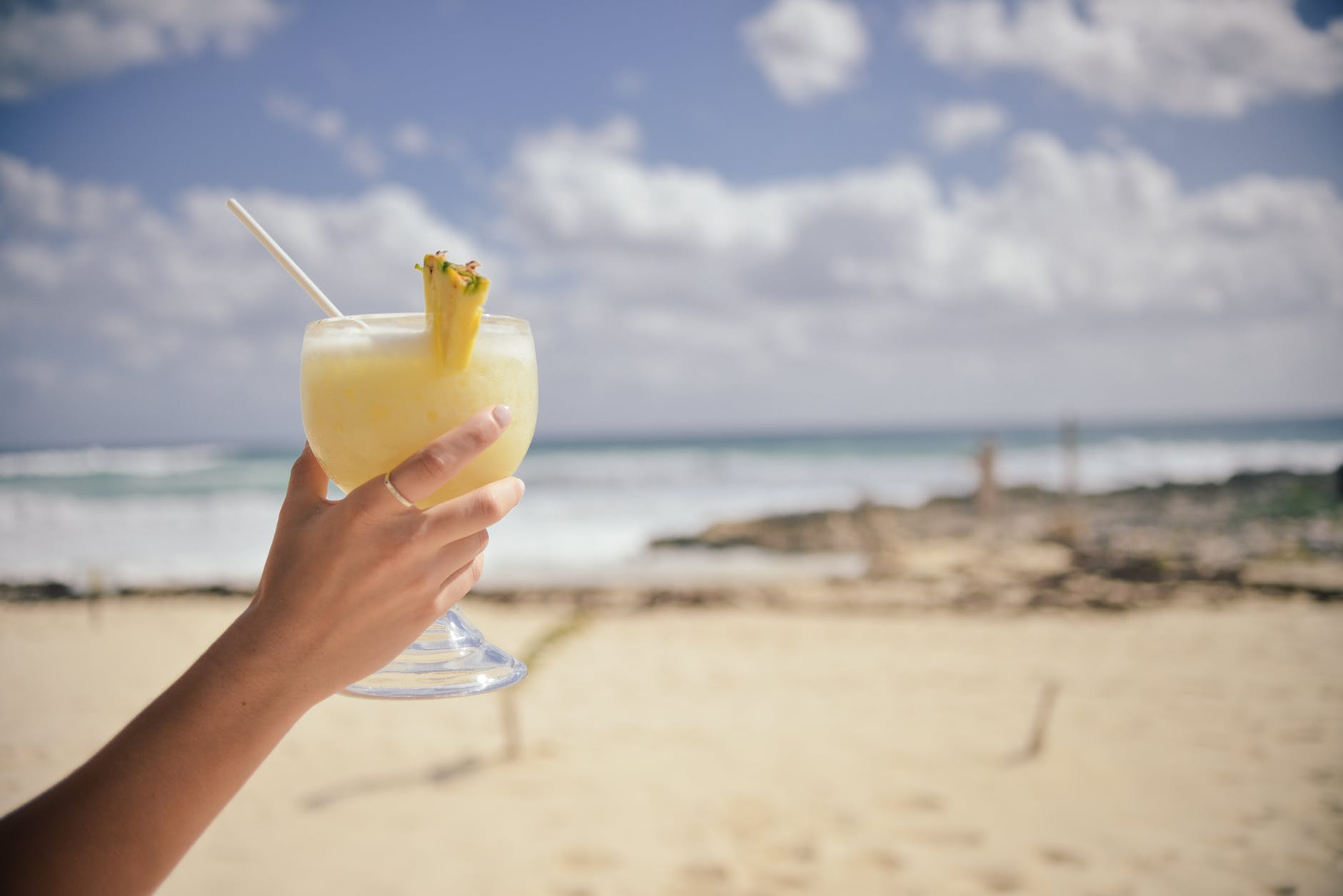 Lady holding a cocktail with a sandy beach in the background